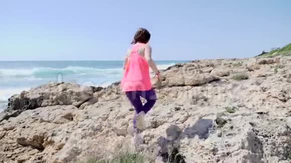 年轻的运动女孩穿着粉红色的衣服在岩石小径上奔跑后射慢动作视频的预览图