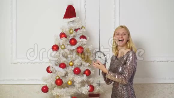 圣诞快乐新年快乐迷人的金发女孩站在圣诞树旁家中挂着时钟微笑着视频的预览图