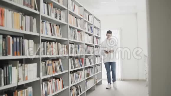 英俊的年轻学生手拿书在书架间行走视频的预览图
