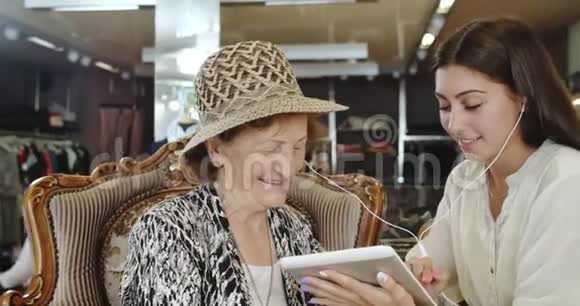 孙女和祖母听音乐通过平板电脑在网上购物视频的预览图