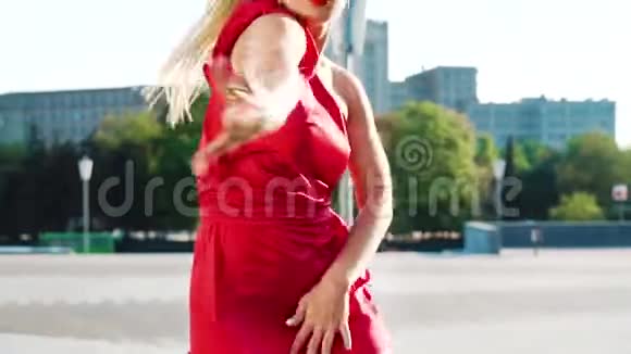漂亮的金发女人穿着红色连衣裙在外面的大街上慢动作跳舞视频的预览图