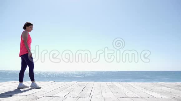 年轻健康的运动女性在海滩上做车轮强浪冲击海岸慢动作视频的预览图