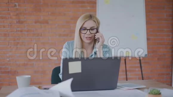 成功的商务女性在她自己的办公室里一边坐在桌子旁一边打电话成功的概念4K视频的预览图