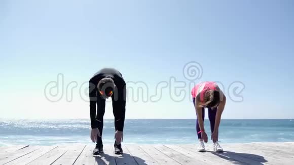 在阳光明媚的沙滩上做伸展运动的年轻男女视频的预览图
