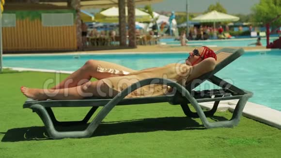 一位穿着浴袍的年轻女子在游泳池附近的一张躺椅上晒太阳视频的预览图