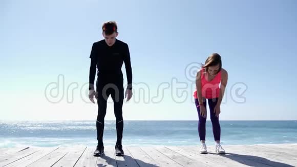 年轻健康的男人和女人在阳光明媚的海滩上做伸展运动慢动作视频的预览图