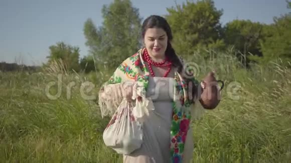 美丽的超重女人走在狂野的高草与土罐在绿色的夏天的田野美丽美丽视频的预览图