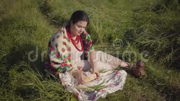 美丽的超重女人坐在草地上吃一块新鲜的面包传统健康食品视频的预览图