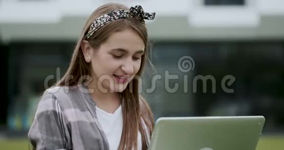 白种人女人一边打字一边坐在草坪上迷人的微笑女孩在外面用笔记本电脑积极情绪视频的预览图