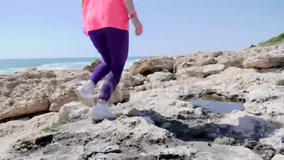 年轻健康的女人沿着海滩经营岩石小径小径在岩石上奔跑慢动作后射视频的预览图