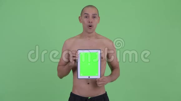 快乐秃顶的多民族赤膊男子展示数码平板电脑看上去很惊讶视频的预览图