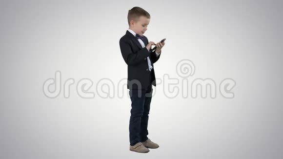 穿着优雅西装在渐变背景下玩手机的小男孩视频的预览图