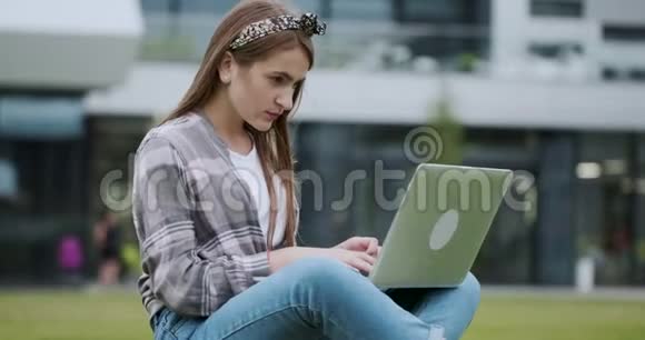 一个聪明的女孩在户外工作坐在草坪上靠大楼的特写镜头视频的预览图