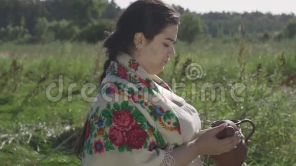 可爱的超重妇女喜欢喝新鲜牛奶从土罐在绿色的夏季田野美丽的风景视频的预览图