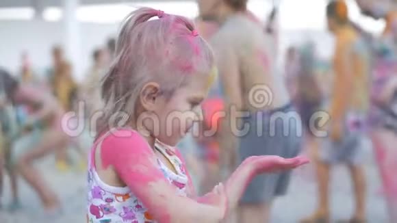 一个可爱的小女孩通过玩五颜六色的颜料和沙子来参加油漆节他的脸和衣服视频的预览图