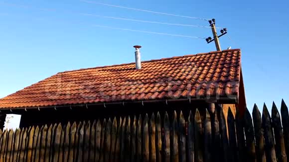 由锋利的木桩制成的栅栏有红色瓷砖屋顶和蓝色晴空的木屋晴天视频的预览图