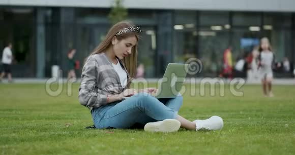 年轻的女学生在露天坐时使用笔记本电脑女孩用笔记本电脑查找资料视频的预览图