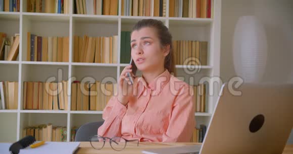 年轻漂亮的女商人坐在笔记本电脑前愉快地打着电话的特写镜头视频的预览图