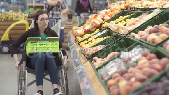 在超市里坐轮椅购物的残疾妇女选择水果并把它们放在一个包裹里视频的预览图