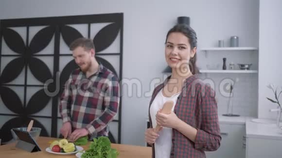 厨房里幸福微笑的女孩画像满意的女人看着从蔬菜中准备有益健康食物的男人视频的预览图