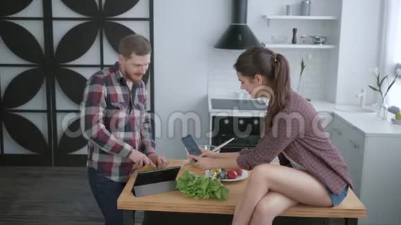 快乐有趣的男孩和女孩在手机上自拍在烹饪健康蔬菜沙拉时做鬼脸视频的预览图
