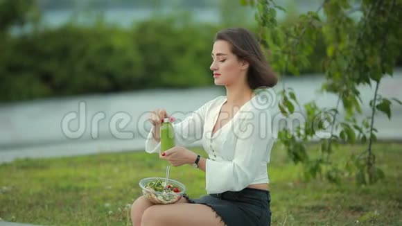 美丽的女人坐在公园里吃沙拉喝冰沙视频的预览图