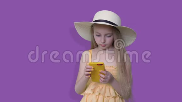 戴帽子的夏天女孩在紫色背景下看手机少年少女夏季服装和帽子使用视频的预览图