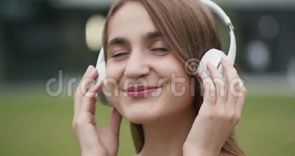 快乐的年轻女子在街上欣赏音乐跳舞快乐的年轻女子听音乐在城市戴耳机视频的预览图