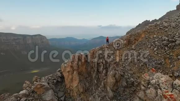 一位背着背包的女游客站在一座高岩石山的悬崖边上看着这座山视频的预览图