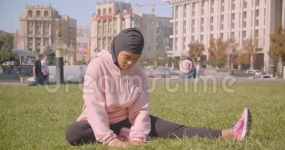 年轻漂亮的戴头巾的非裔美国穆斯林女孩坐在城市的草地上的特写照片视频的预览图