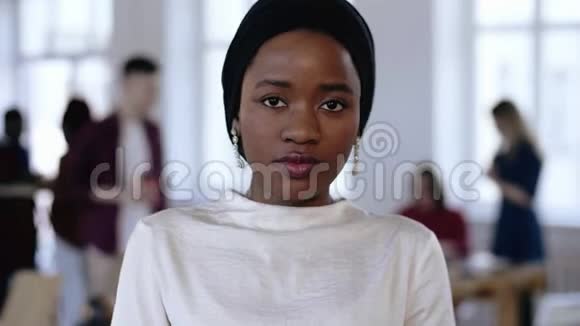 穿着民族头巾的年轻严肃的非洲企业经理女士看着镜头在时髦的阁楼办公室微笑视频的预览图