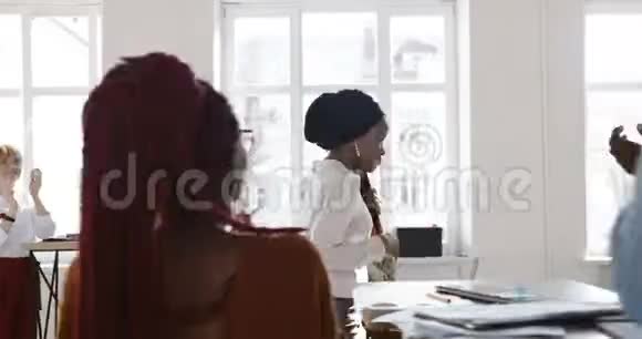 快乐的年轻非洲商务女性头上裹着头巾走在现代化的办公室里受到同事的欢迎和欢呼视频的预览图