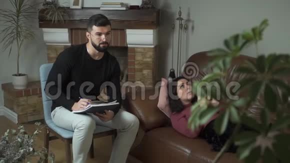 年轻漂亮的高加索女人躺在沙发上和男性心理学家交谈专业精神分析师视频的预览图