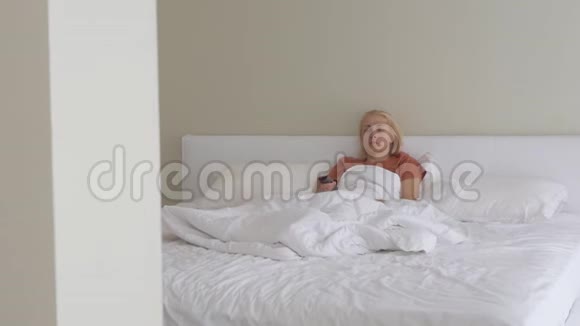 一个女人躺在床上脸上带着一张悲伤的病态她打开电视遥控器视频的预览图