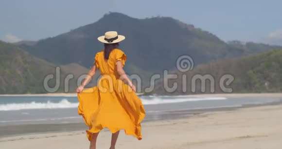苗条的女孩穿着黄色的衣服戴着草帽在沙滩上奔跑在热带下缓慢的运动良好的心情视频的预览图