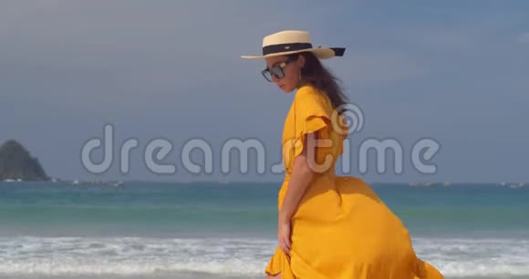 下午穿着黄色衣服和草帽的年轻女子在沙滩上散步心情舒畅视频的预览图