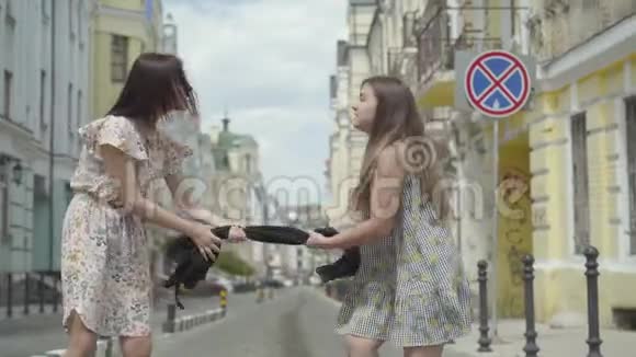 两个时髦的女孩拿着黑色的裙子把它拉到街上的两边购物概念视频的预览图