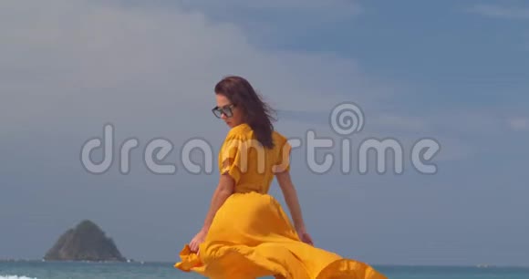 穿着黄色长裙的漂亮女孩走在大海上海浪和风吹起了她的头发和一条轻盈的裙子视频的预览图