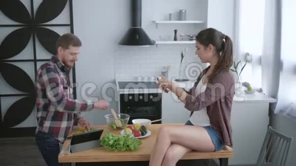 饮食快乐的男人准备健康的素食早午餐女孩坐在厨房的桌子上手机在里面视频的预览图