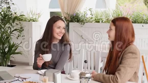 两个年轻女孩边看边喝茶在午餐时慢动作愉快地交谈视频的预览图