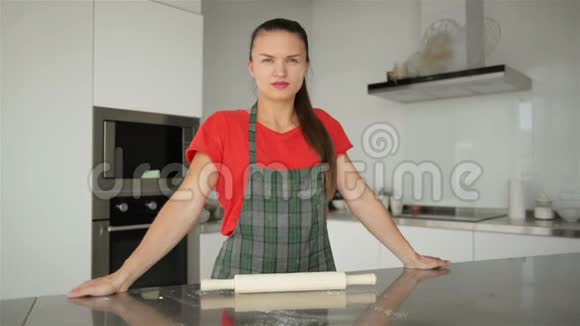 年轻的白人家庭主妇穿着条纹围裙厨房背景上隔离的红色T恤美丽的肖像视频的预览图