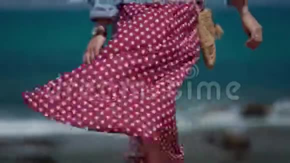穿着红色波尔卡多礼服的年轻女子赤着脚走在海边的石栅栏上后景女性特写视频的预览图