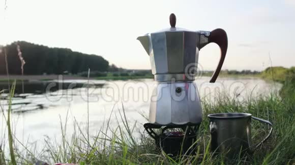带有金属杯的间歇喷泉咖啡机在池塘背景下的多燃料Primus燃烧器上加热视频的预览图