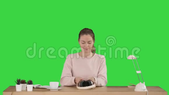 年轻微笑的女人戴上耳机在绿色屏幕上听音乐Chroma键视频的预览图