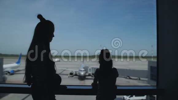 两个姐妹的剪影站在机场候机室的窗口观看飞机视频的预览图