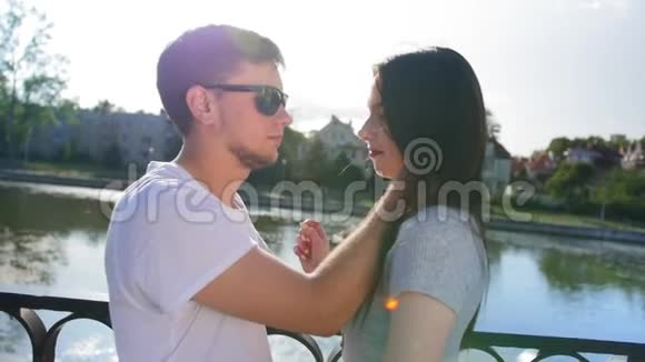 在池塘附近的绿色夏季公园里的浪漫情侣男人抚摸女朋友脸享受她心爱的爱情快乐视频的预览图