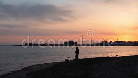 码头上令人难以置信的粉红色日落前面是带着钓竿的孤独渔夫视频的预览图