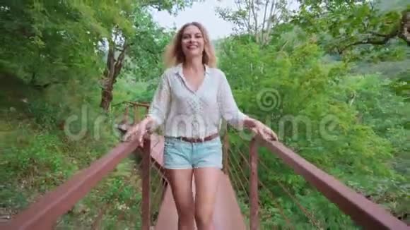 一位开朗风趣的年轻女子金发碧眼沿着峡谷峡谷上的长长的铁桥漫步旅游女郎滚滚而来视频的预览图