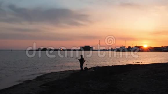 孤独男人的剪影带着钓鱼竿站在空荡荡的海滩上地平线上有粉红色的日落日落时分钓鱼人剪影视频的预览图