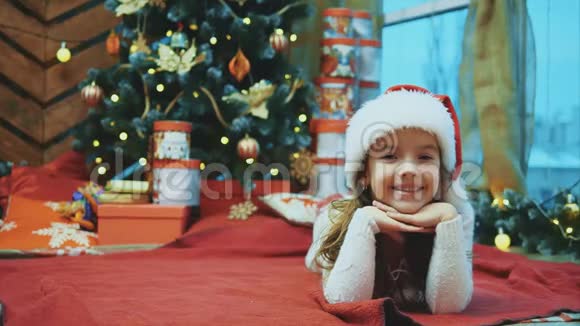 圣诞老人躺在圣诞树下的红毯子上双腿穿着红袜子看着摄像机视频的预览图